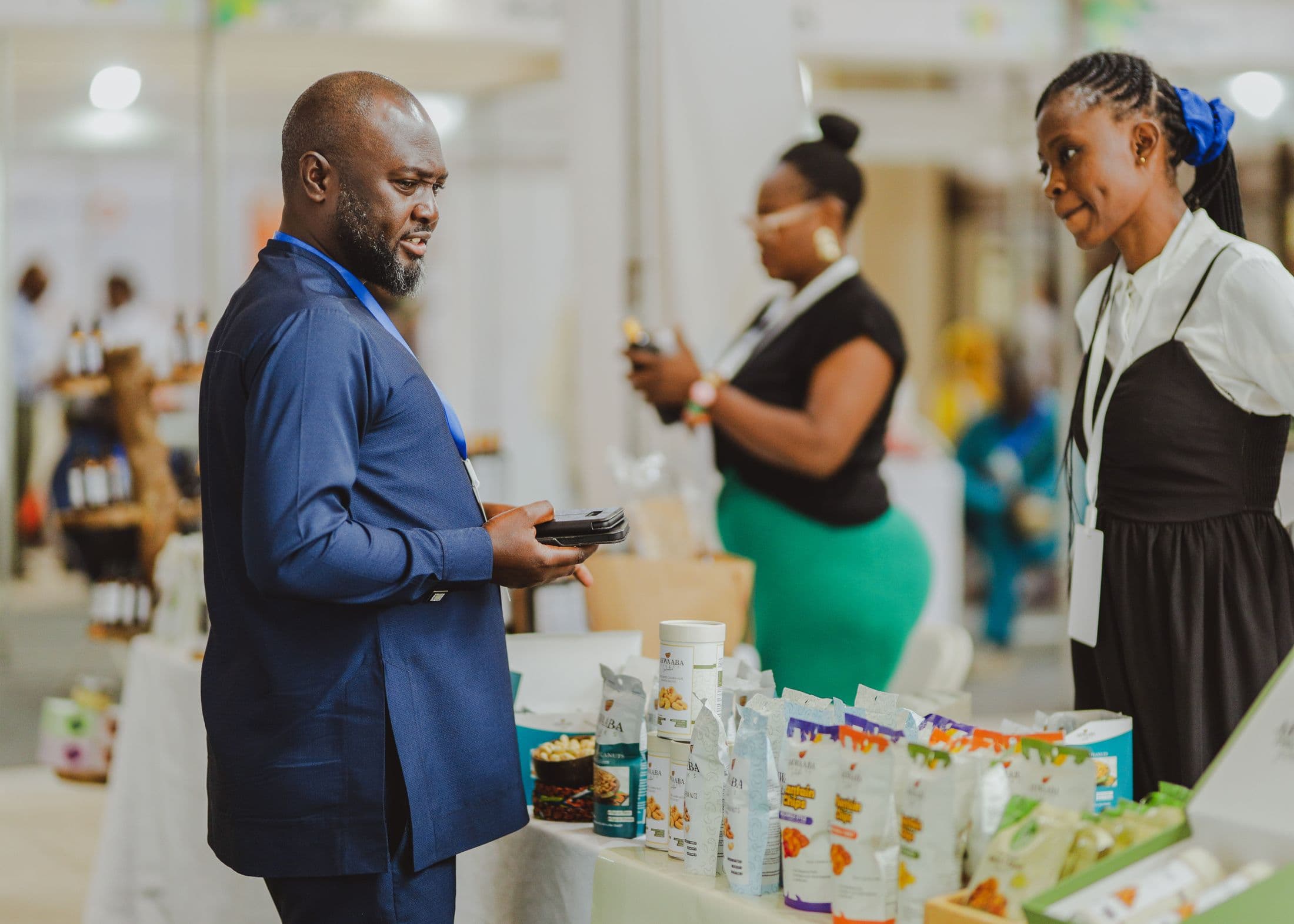 An exhibitor in a blue agbada talks with a stallholder at a trade show in Accra